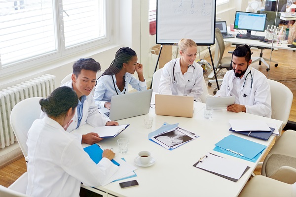 Group of clinicians sat around a table with with laptops and a whiteboard in the background